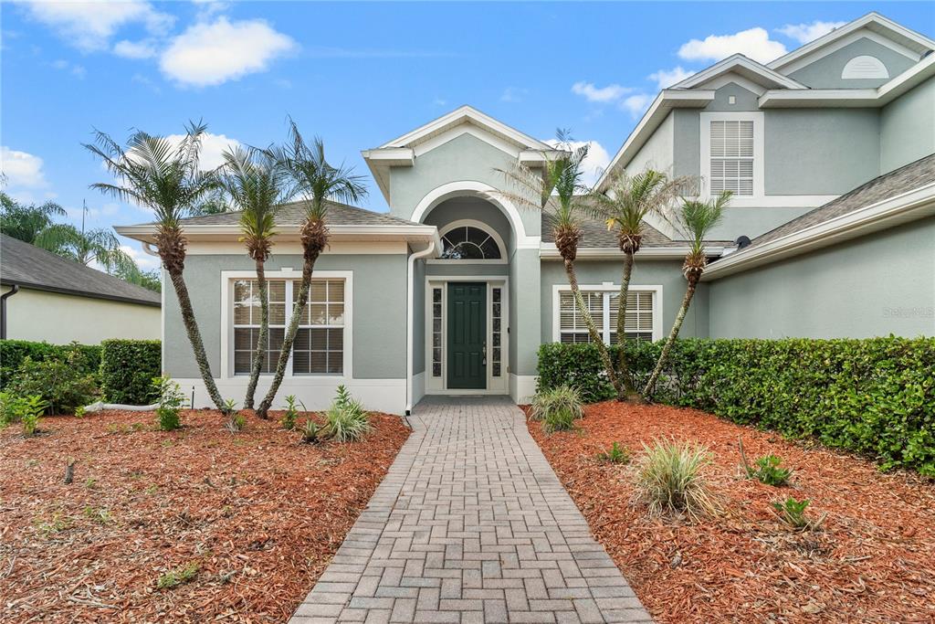 A paved walkway leads to the front entrance of a light green house with palm trees — 3463 FOREST RIDGE LANE, KISSIMMEE, FL
