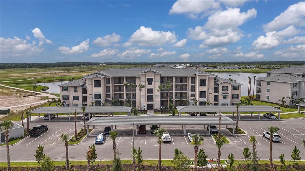 An aerial view shows a multi-story apartment building with covered parking spaces and a pond — 19140 SCALLOP LOOP UNIT 102, LAKEWOOD RANCH, FL