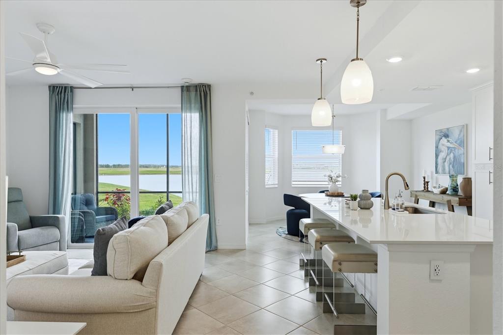 An open-concept living area features a kitchen with a white island and a water view — 19140 SCALLOP LOOP UNIT 102, LAKEWOOD RANCH, FL