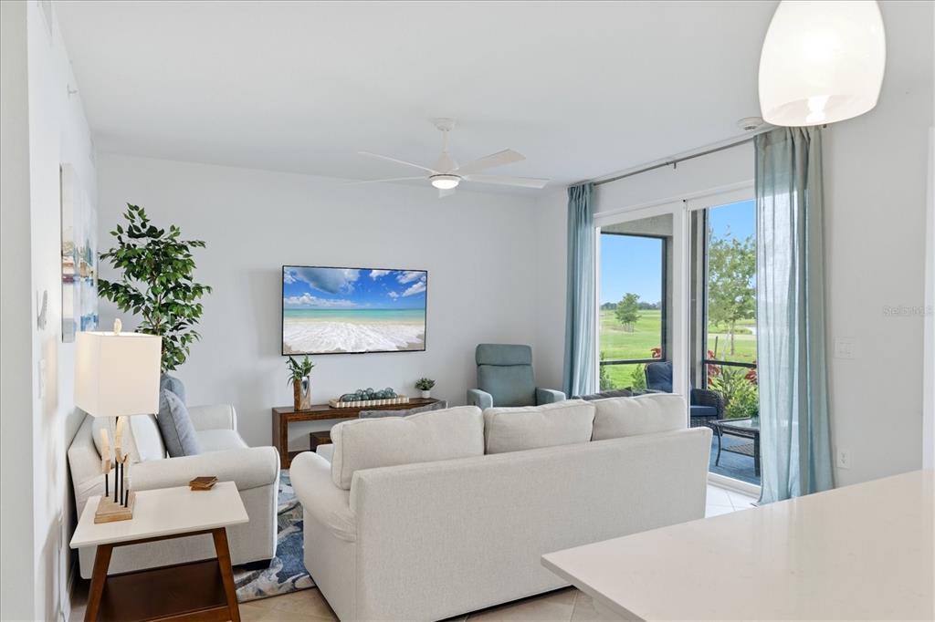 A living room features a white sofa, television, ceiling fan, and sliding doors to a patio — 19140 SCALLOP LOOP UNIT 102, LAKEWOOD RANCH, FL