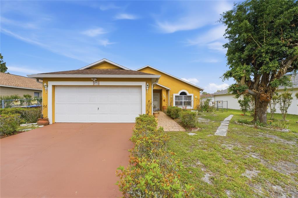 A yellow single-story house with a white garage door and a paved walkway — 675 BASINGSTOKE COURT, POINCIANA, FL