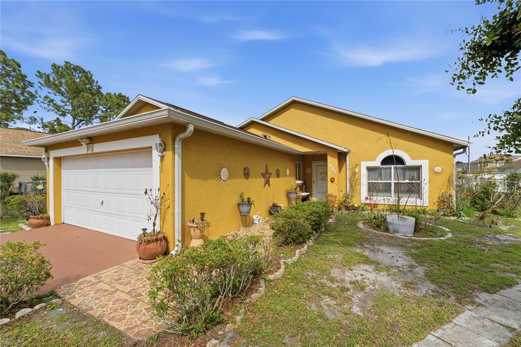 A yellow single-story house features a white garage door and a front-facing arched window — 675 BASINGSTOKE COURT, POINCIANA, FL