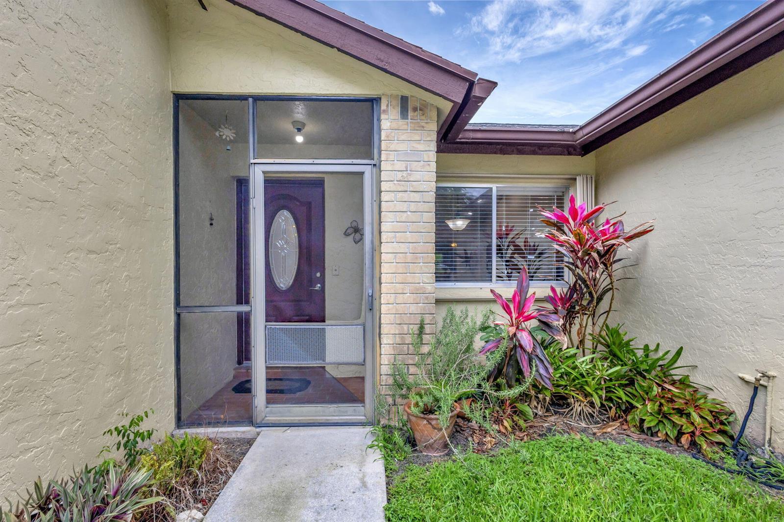 The exterior of a home features a screened entryway, a brick column, and landscaping — 178 Ramblewood Circle, Royal Palm Beach FL 33411, ROYAL PALM BEACH, FL