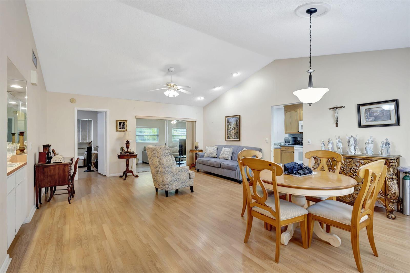An open-concept living and dining area features light wood flooring, vaulted ceilings, and neutral walls — 178 Ramblewood Circle, Royal Palm Beach FL 33411, ROYAL PALM BEACH, FL