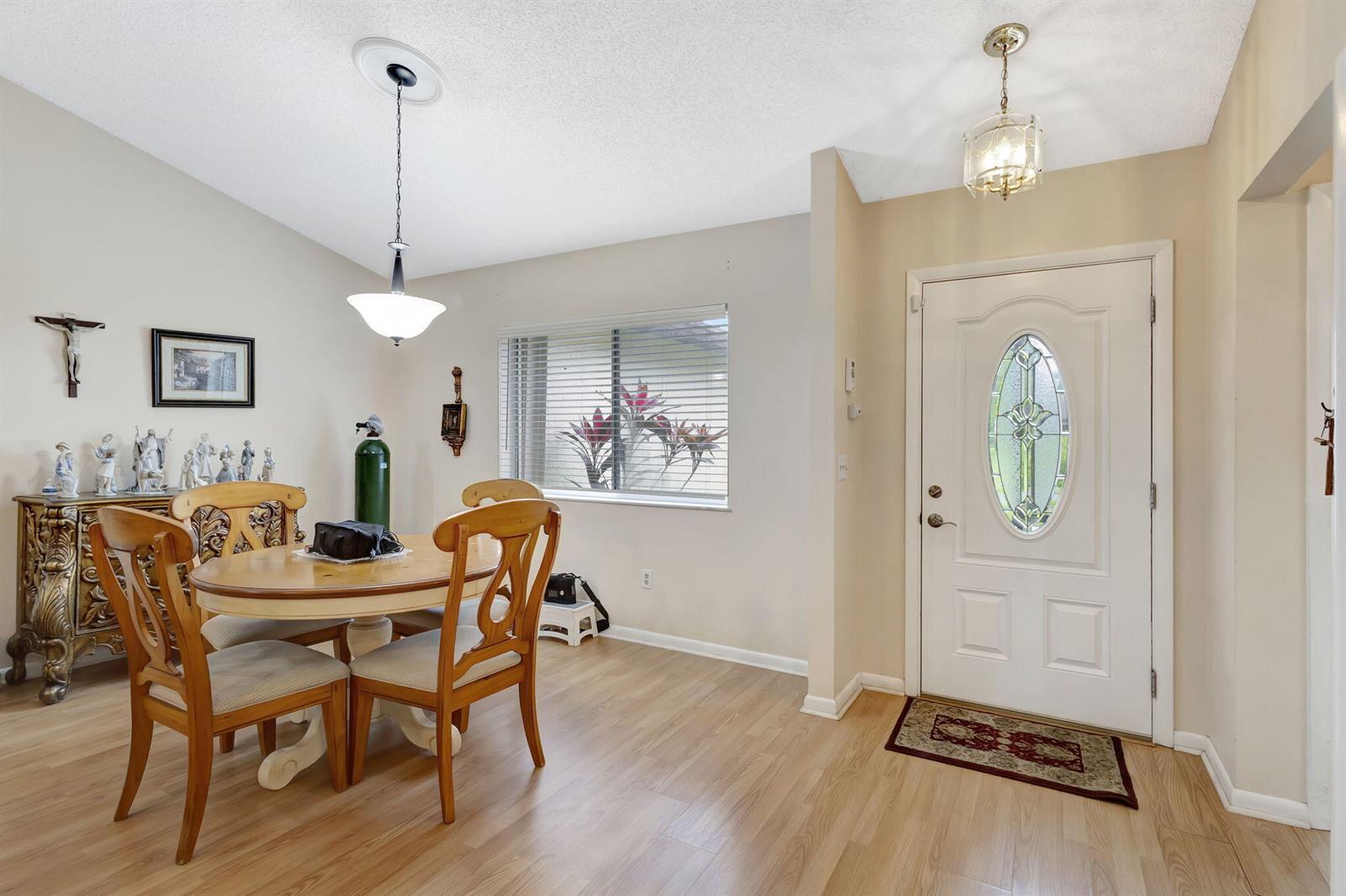 A dining area with a wooden table and chairs sits beside a white front door — 178 Ramblewood Circle, Royal Palm Beach FL 33411, ROYAL PALM BEACH, FL