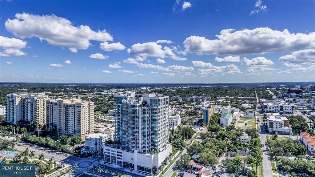 An aerial view shows a modern high-rise apartment building surrounded by urban development and trees — 555 QUAY COMMON UNIT 2001, SARASOTA, FL