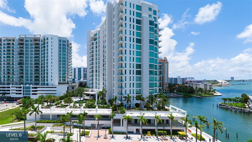 An exterior view shows a tall white residential building with balconies overlooking a waterfront area — 555 QUAY COMMON UNIT 2001, SARASOTA, FL