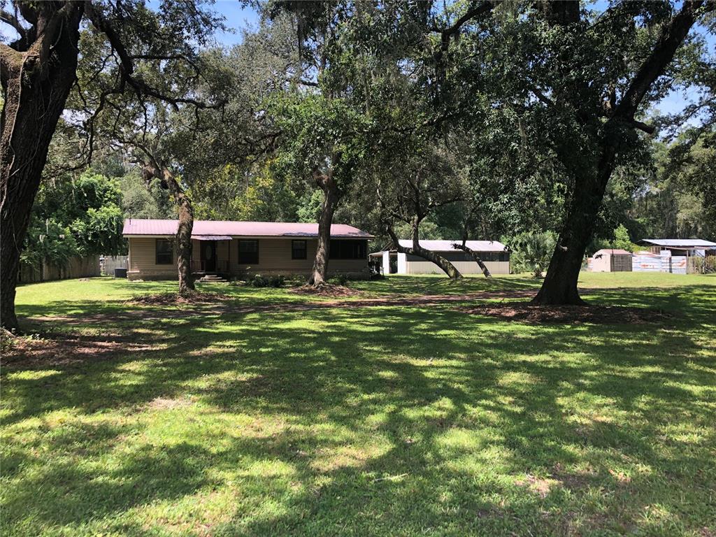 A single-story house with a metal roof sits on a large, tree-shaded grassy lot — 136 S COMMERCIAL STREET, COLEMAN, FL