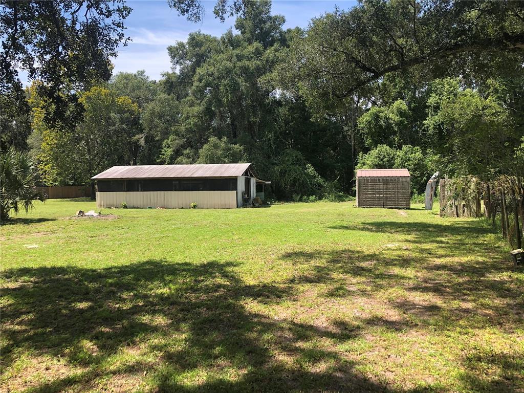 A large grassy yard features a long, light-colored shed and a smaller storage structure — 136 S COMMERCIAL STREET, COLEMAN, FL
