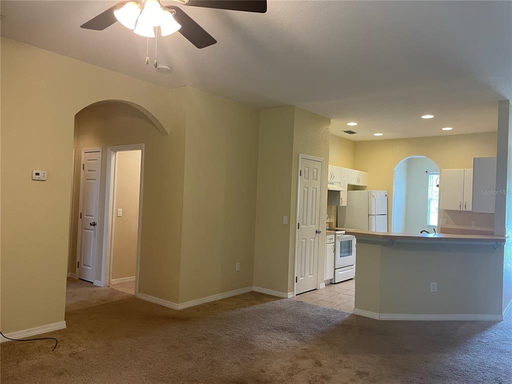 A living room with carpeted floors leads into a kitchen with white cabinets and appliances — 1818 GOVERNOR AVENUE, NORTH PORT, FL