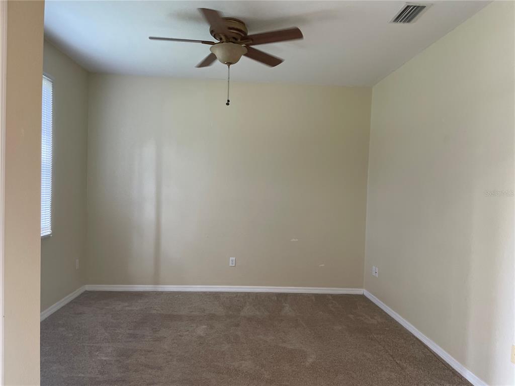 An empty room features beige walls, brown carpeting, and a ceiling fan — 1818 GOVERNOR AVENUE, NORTH PORT, FL