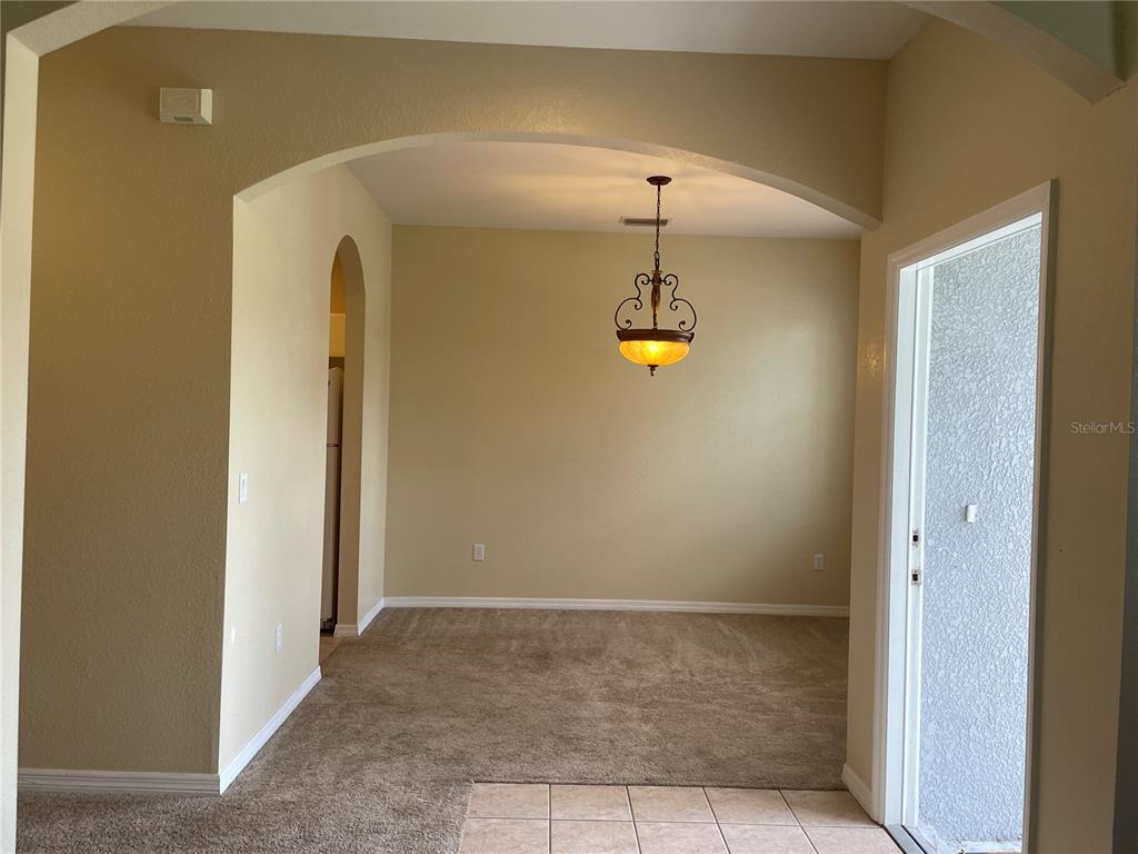 A dining area features beige carpet, tan walls, an arched entryway, and a hanging light fixture — 1818 GOVERNOR AVENUE, NORTH PORT, FL