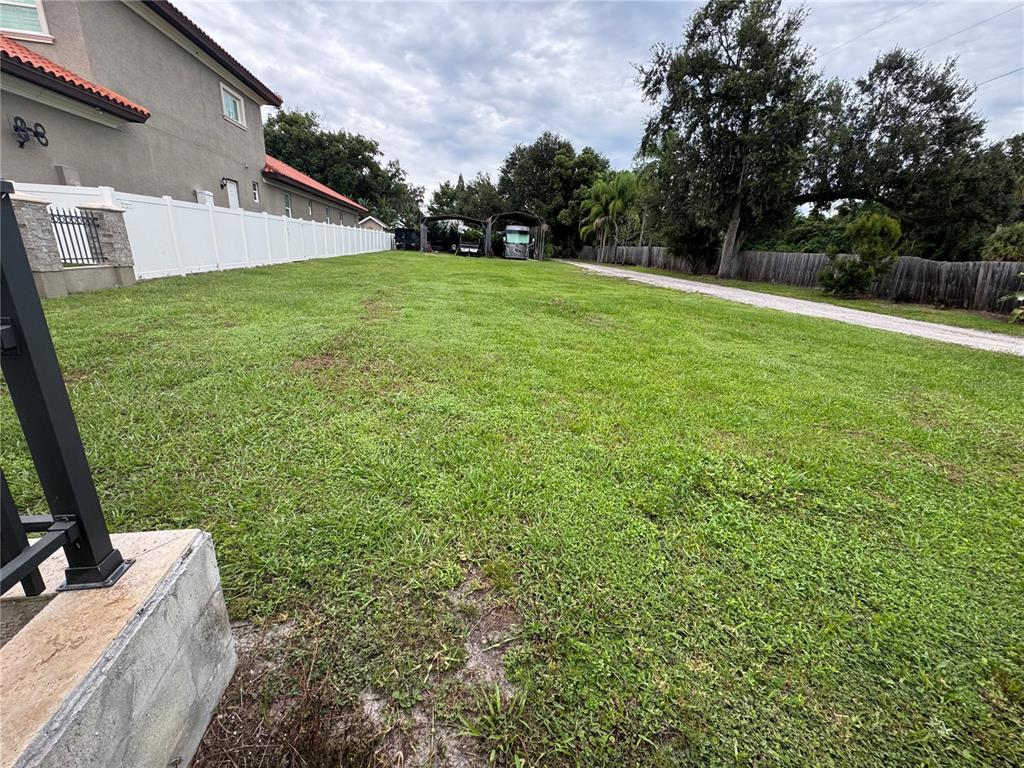 A large, grassy backyard features a white vinyl fence and a gravel driveway — 2065 W BEARSS AVENUE, TAMPA, FL