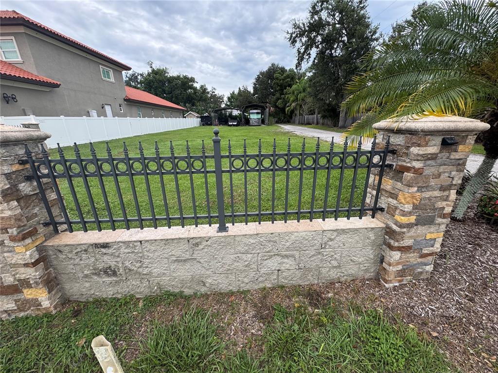 A stone and metal fence stands in front of a grassy yard with a house — 2065 W BEARSS AVENUE, TAMPA, FL