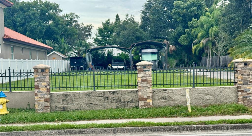 A fenced vacant lot features stone pillars, a concrete wall, and two metal carports — 2065 W BEARSS AVENUE, TAMPA, FL