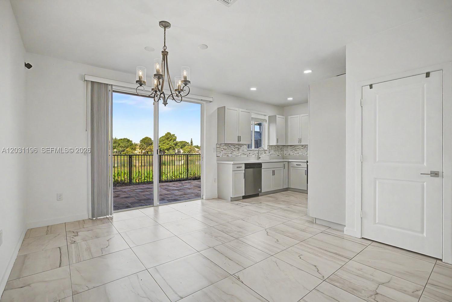 A kitchen and dining area features white cabinets, tile flooring, and a sliding glass door — 1014 SE 23rd Ave, Homestead FL 33035, HOMESTEAD, FL