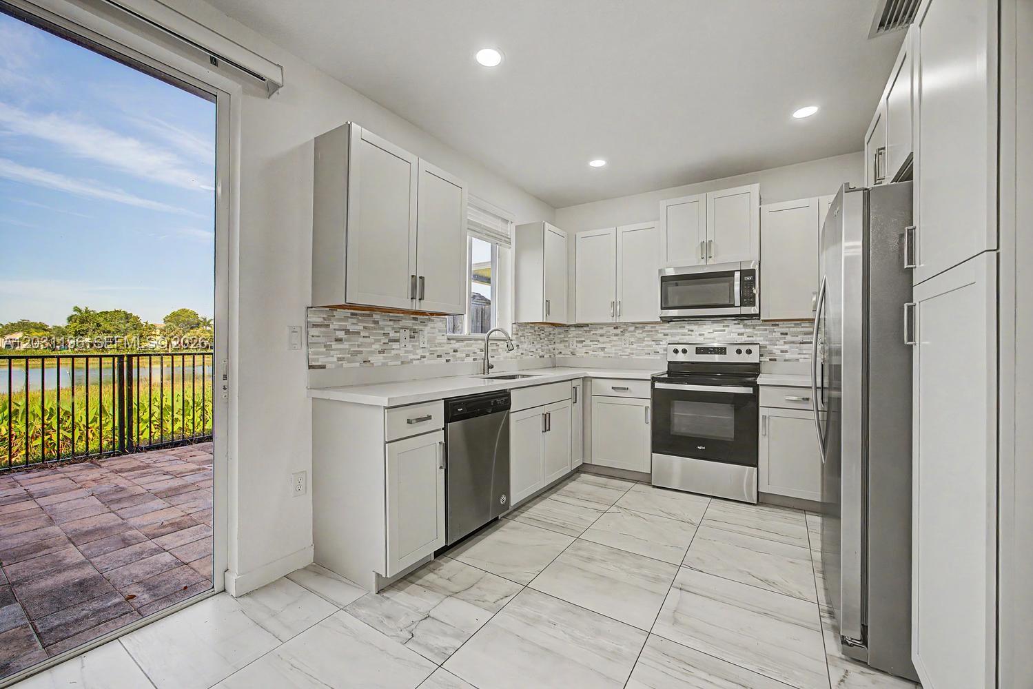 A modern kitchen features white cabinetry, stainless steel appliances, and a view of a lake — 1014 SE 23rd Ave, Homestead FL 33035, HOMESTEAD, FL