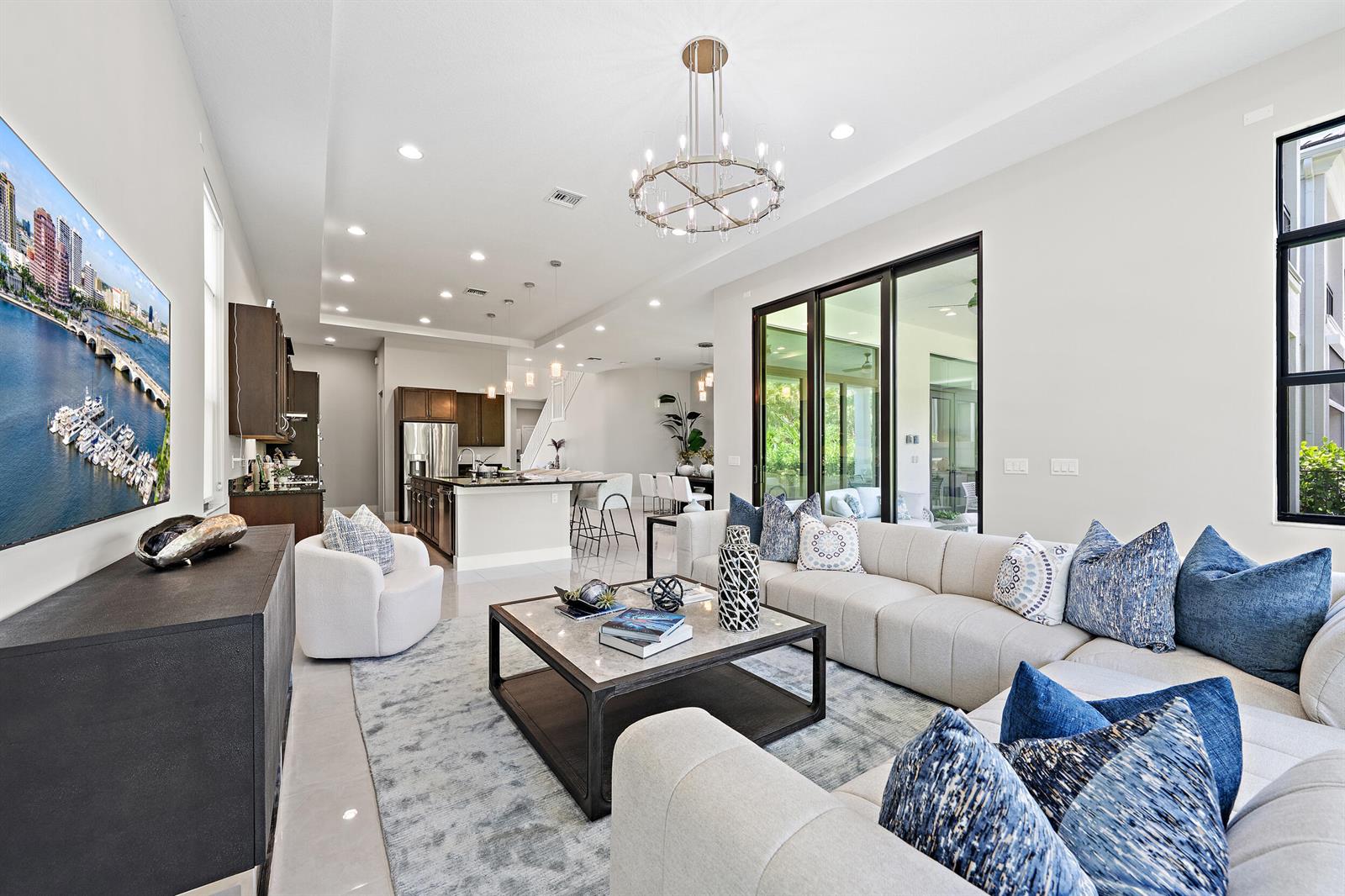A modern open-concept living room features a large sectional sofa, kitchen island, and chandelier — 13358 Artisan Circle, Palm Beach Gardens FL 33418, PALM BEACH GARDENS, FL