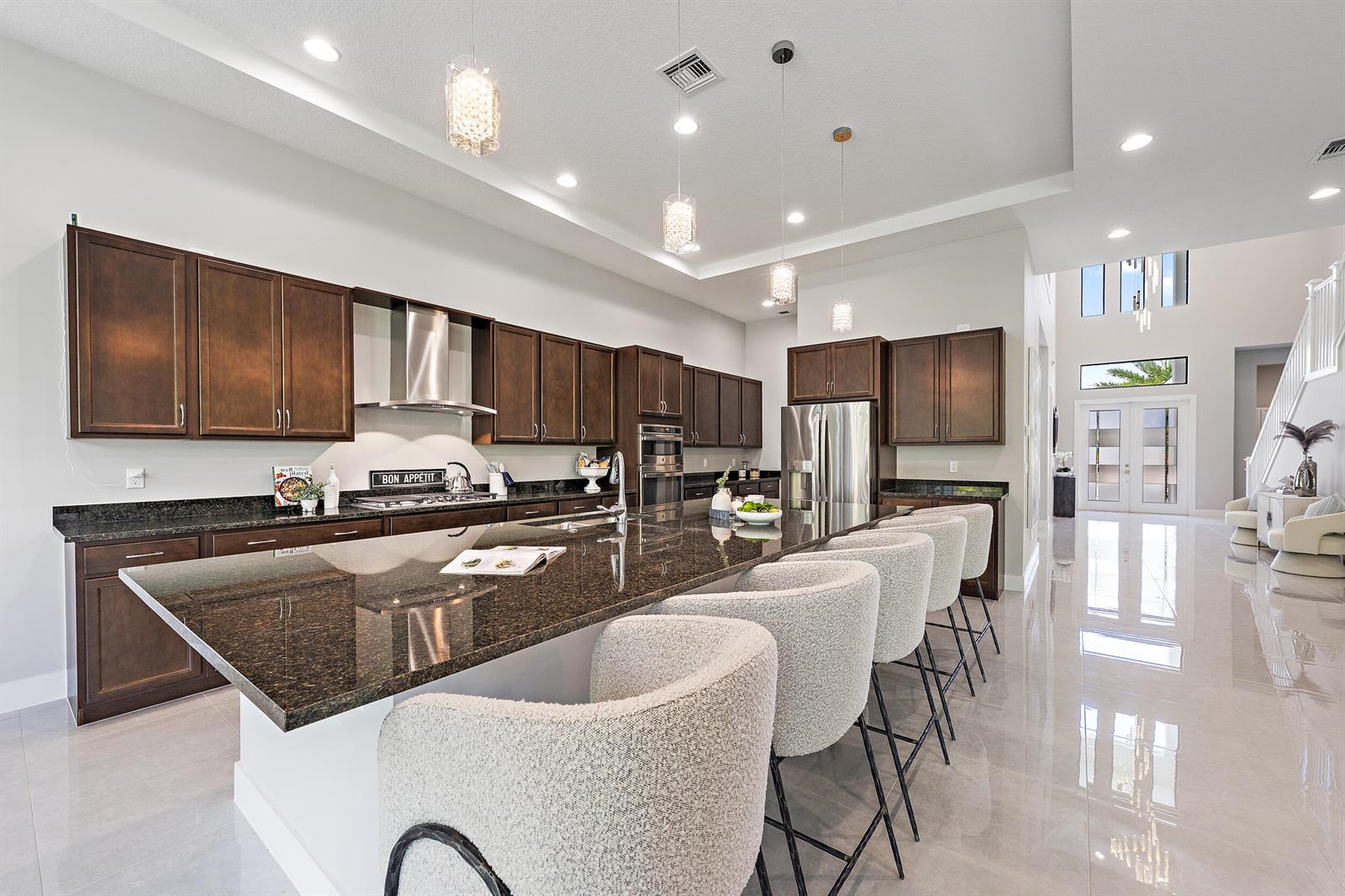 A modern kitchen features dark wood cabinets, granite countertops, a large island, and bar stools — 13358 Artisan Circle, Palm Beach Gardens FL 33418, PALM BEACH GARDENS, FL