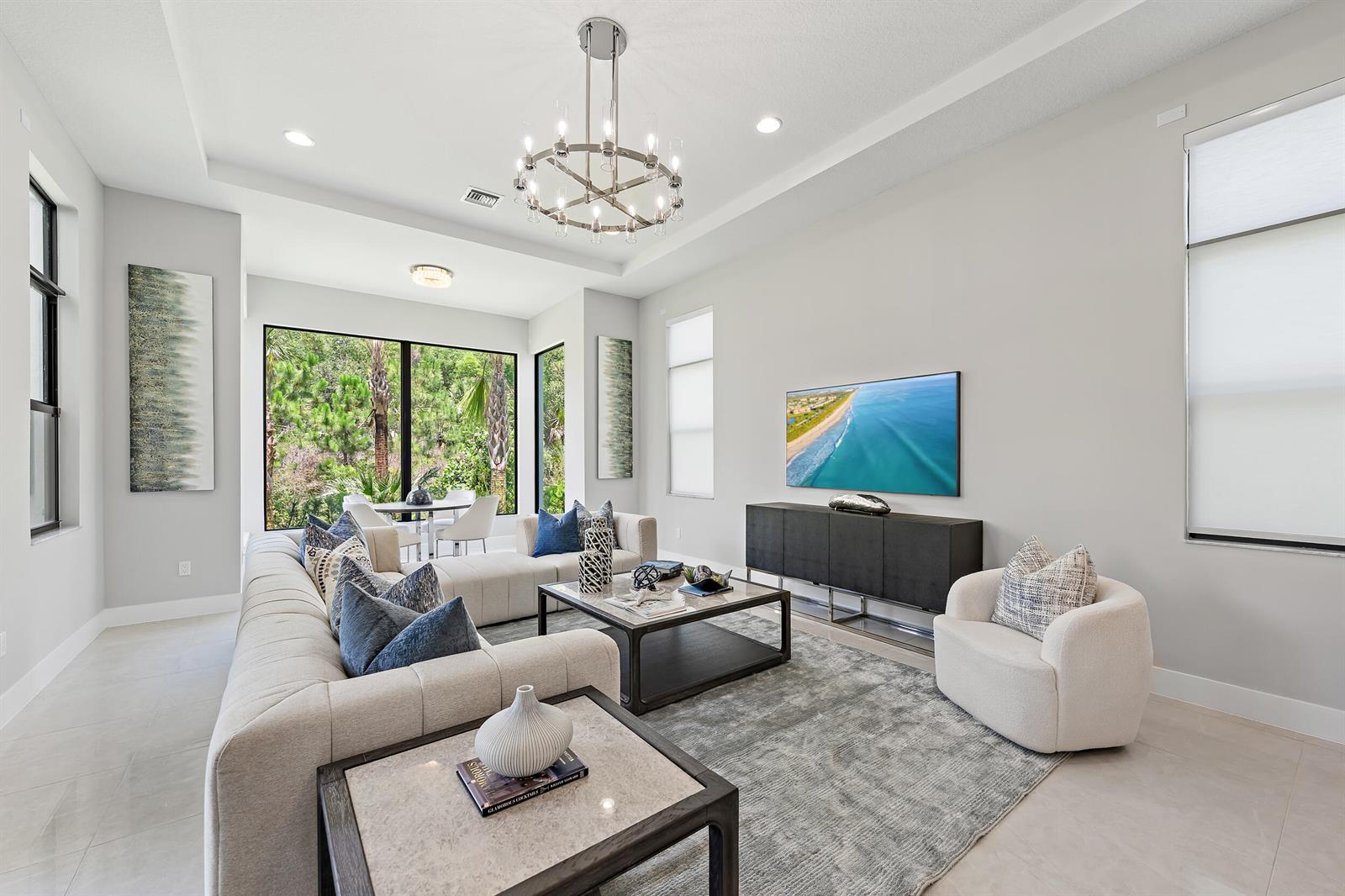 A modern living room features a large sectional sofa, a chandelier, and a wall-mounted television — 13358 Artisan Circle, Palm Beach Gardens FL 33418, PALM BEACH GARDENS, FL