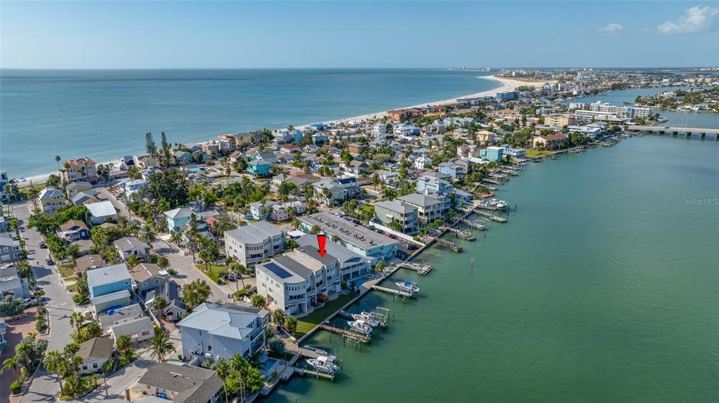 An aerial view shows a coastal neighborhood with houses along a bay and beach — 8575 SUNSET COURT, TREASURE ISLAND, FL