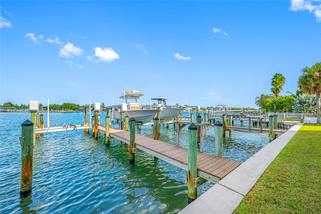 A wooden boat dock with two boats on lifts extends into a calm canal — 8575 SUNSET COURT, TREASURE ISLAND, FL
