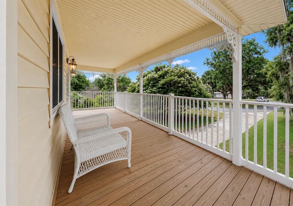 A covered wooden porch features a white wicker chair and white railings overlooking a yard — 8017 MAYS AVENUE, RIVERVIEW, FL