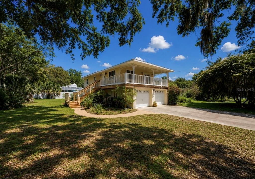 A two-story elevated house with a wrap-around porch, white railings, and a two-car garage — 8017 MAYS AVENUE, RIVERVIEW, FL
