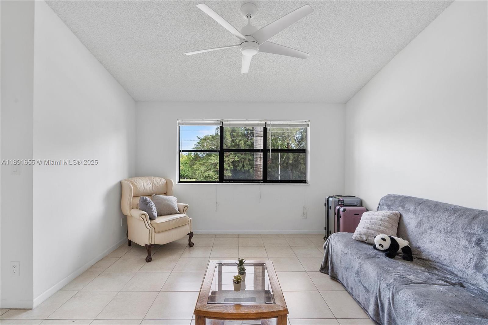 A living room features white walls, tile flooring, a ceiling fan, and a large window — 610 S Park Rd # 1, Hollywood FL 33021, HOLLYWOOD, FL