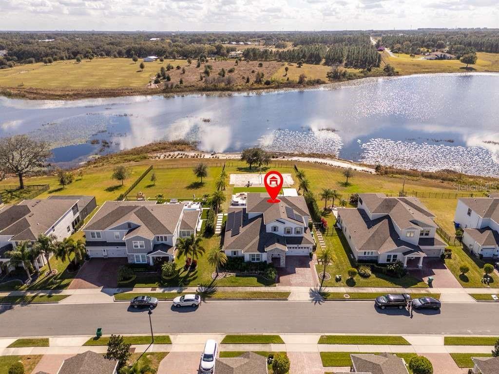 An aerial view shows a suburban house with solar panels located beside a large lake — 16870 SANCTUARY DRIVE, WINTER GARDEN, FL