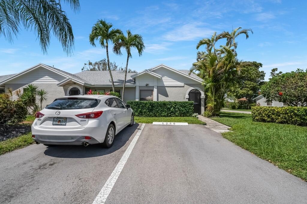 A white car is parked in the driveway of a single-story house with palm trees — 1260 NW 24th Avenue, Delray Beach FL 33445, DELRAY BEACH, FL