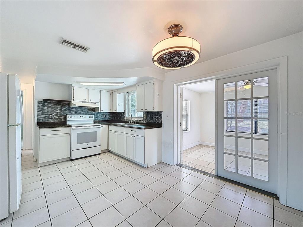 A kitchen with white cabinets, a tiled backsplash, and a white stove, adjacent to a sunroom — 4130 CRESTFIELD AVENUE, HOLIDAY, FL