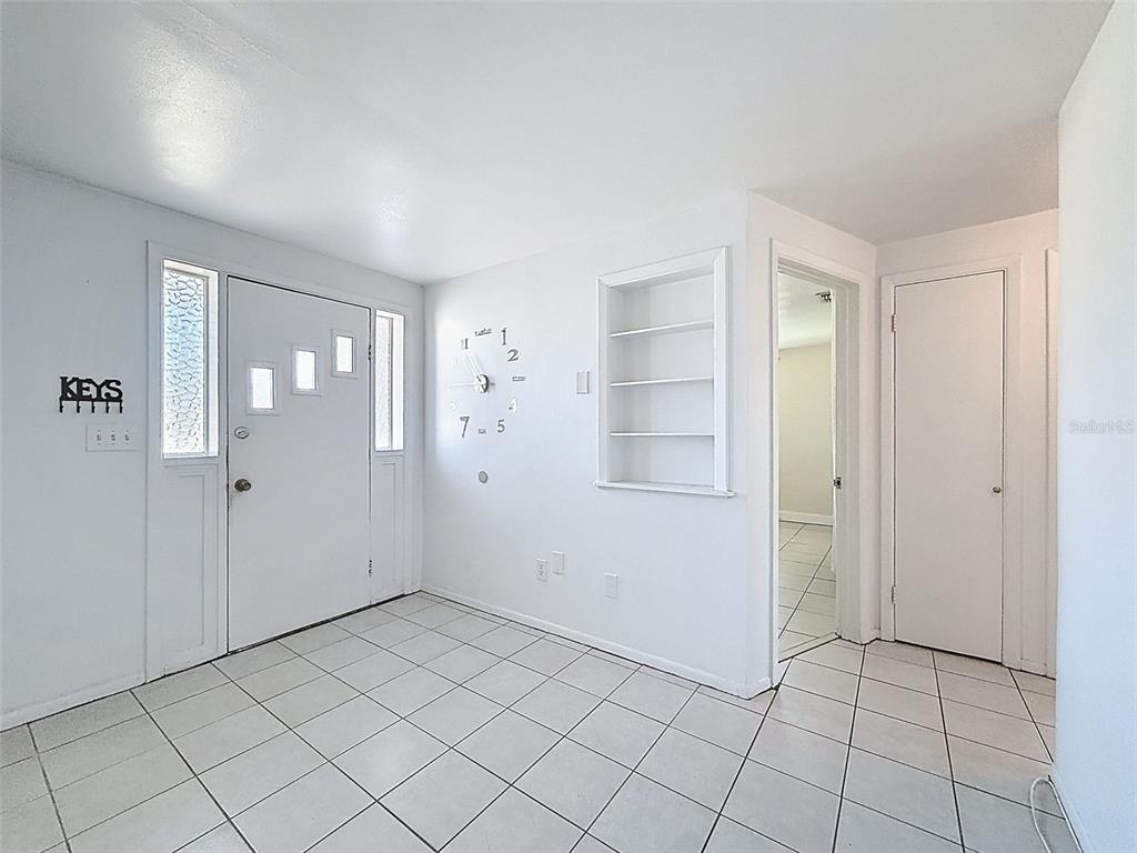 An entryway with white tile floors, a front door, built-in shelving, and a wall clock — 4130 CRESTFIELD AVENUE, HOLIDAY, FL