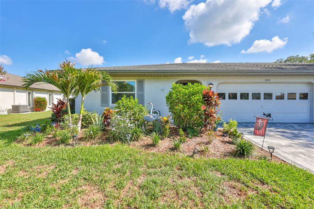 A single-story house with a white stucco exterior, a two-car garage, and a landscaped front yard — 1403 LANGLEY DRIVE, SUN CITY CENTER, FL