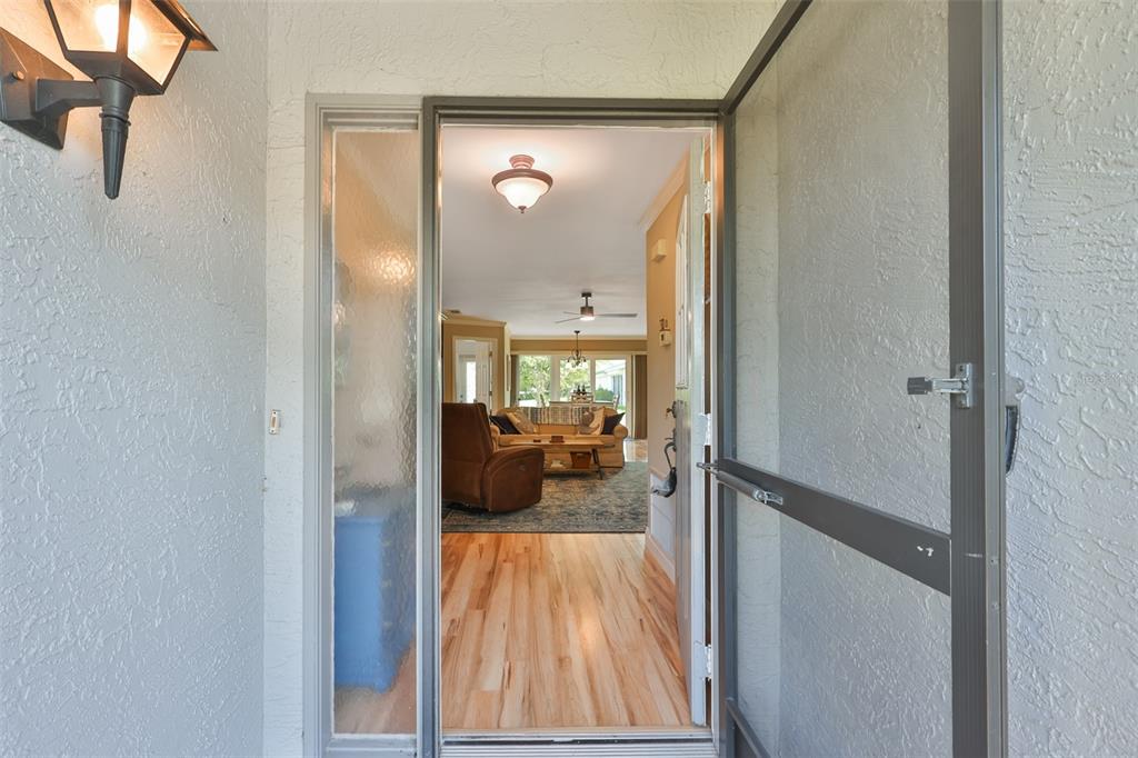 A view through an open screen door into a home with hardwood floors and furniture — 1403 LANGLEY DRIVE, SUN CITY CENTER, FL