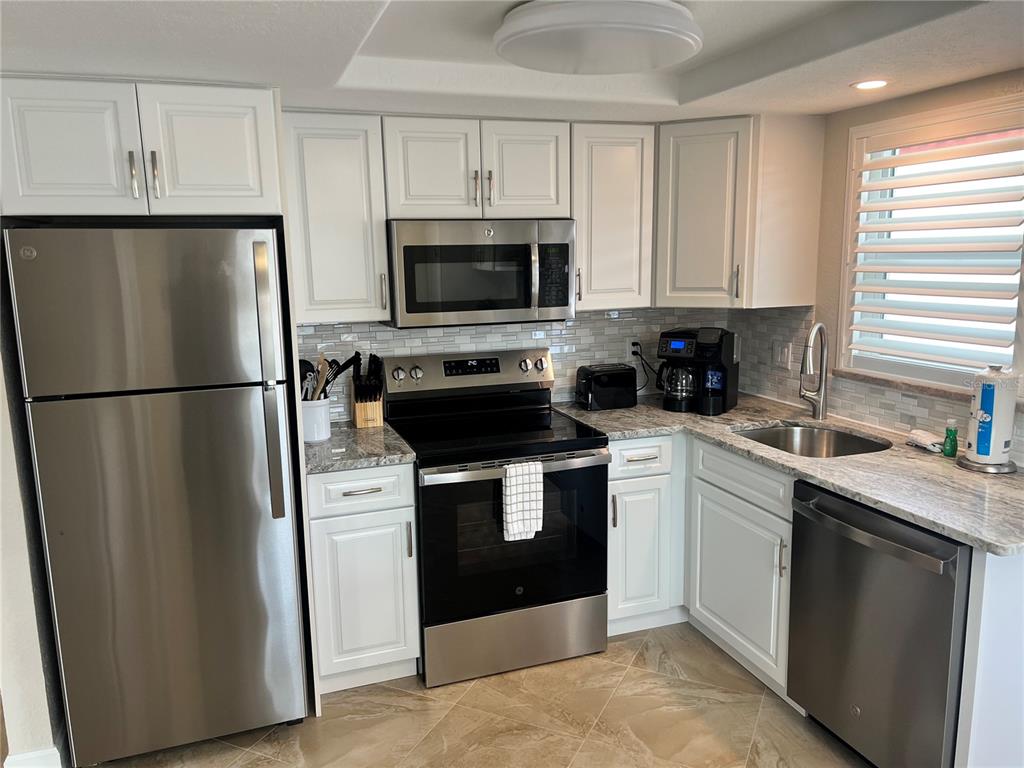 A kitchen features white cabinets, stainless steel appliances, granite countertops, and a tiled backsplash — 6154 MIDNIGHT PASS ROAD UNIT A14, SARASOTA, FL