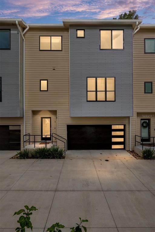A modern three-story townhome with a concrete driveway, dark garage door, and horizontal siding — 2601 SW WILLISTON ROAD UNIT 106, GAINESVILLE, FL