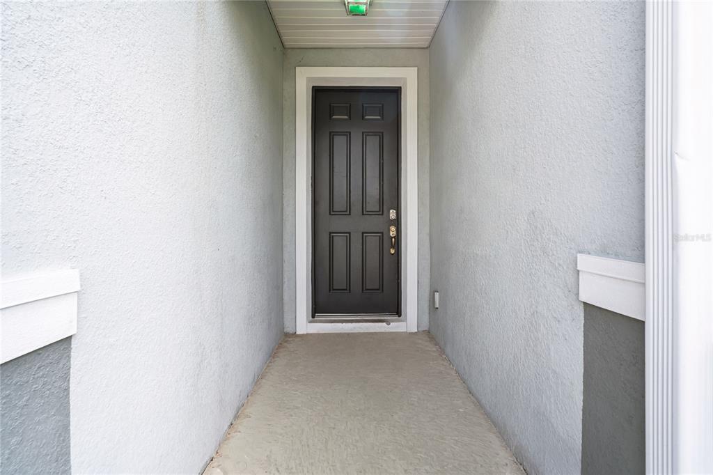 A covered entryway features a dark gray front door with a recessed panel design — 665 CARYA COURT, DELAND, FL