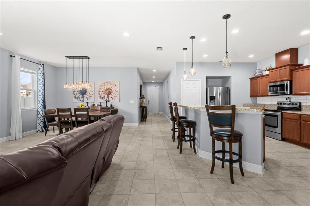 An open-concept kitchen and dining area with tile flooring, wooden cabinets, and a breakfast bar — 665 CARYA COURT, DELAND, FL