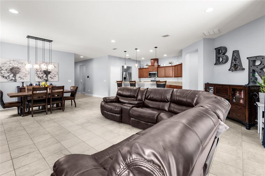 An open-concept living and dining area features a large brown sectional and tile flooring — 665 CARYA COURT, DELAND, FL