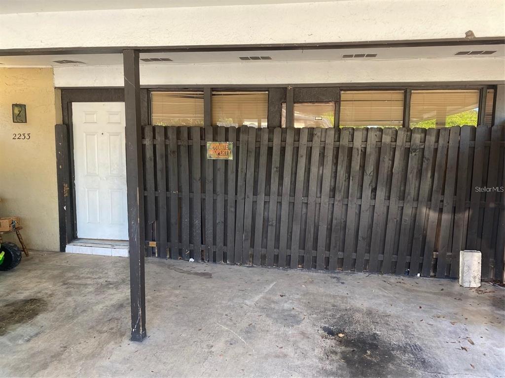 A white door and a dark wooden privacy fence are located under a covered carport — 2233 SILVER PINES PLACE UNIT 506, ORLANDO, FL