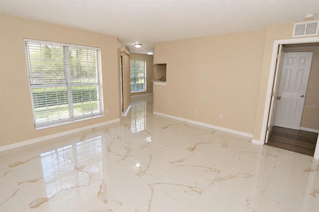 An empty room features white marble-look tile flooring, beige walls, and a white interior door — 8764 MALLARD RESERVE DRIVE UNIT 101, TAMPA, FL