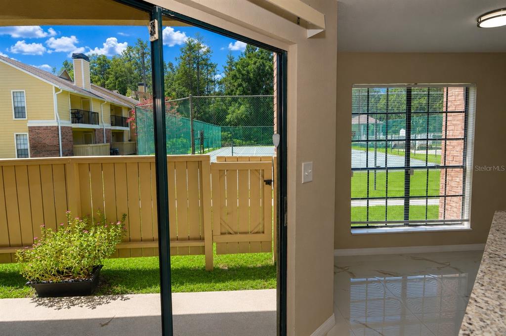 A view from inside a room looking out through a sliding door toward a tennis court — 8764 MALLARD RESERVE DRIVE UNIT 101, TAMPA, FL