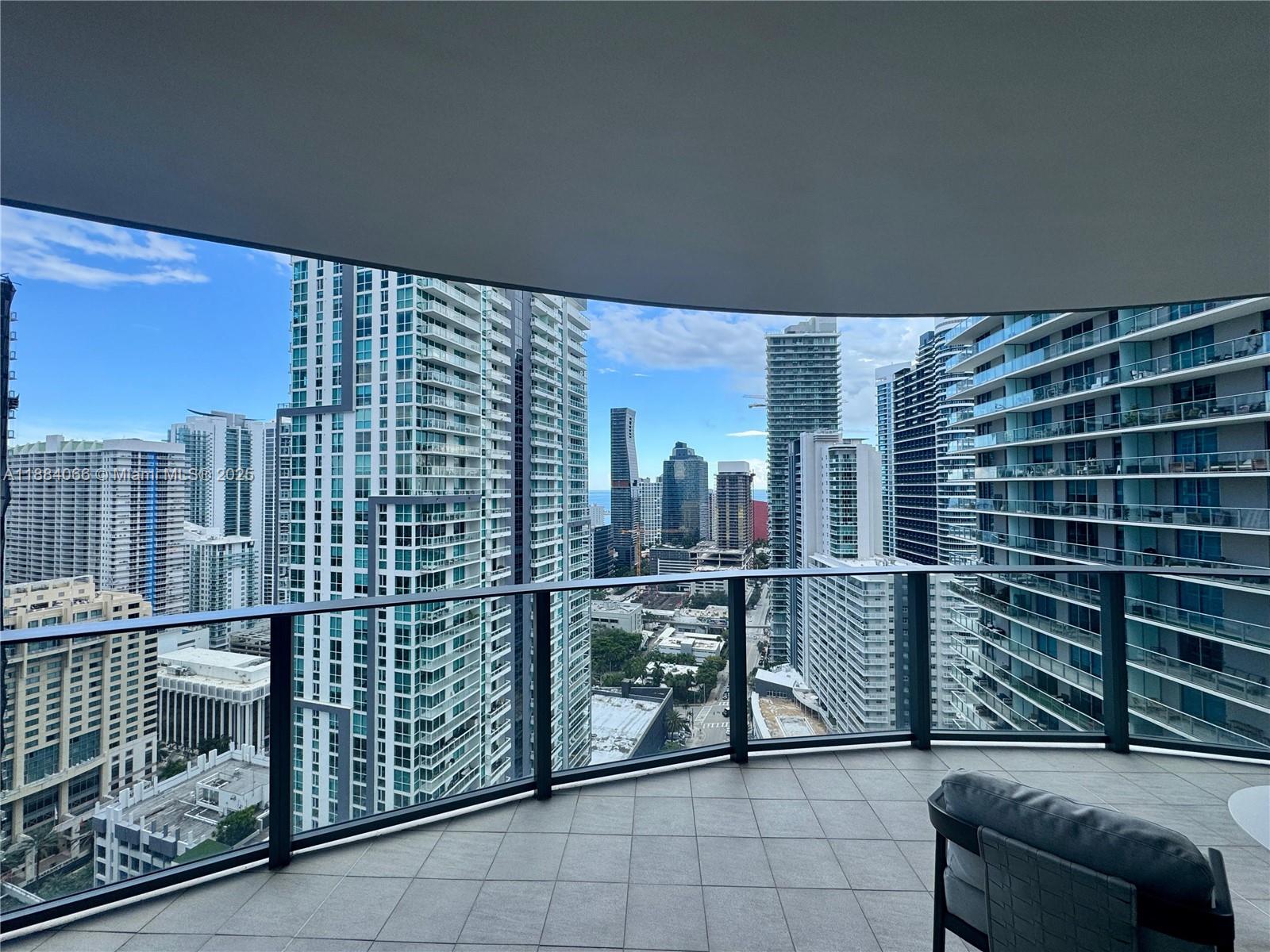 A high-rise balcony with a glass railing overlooks a dense urban skyline — 1000 Brickell Plz # 3302, Miami FL 33131, MIAMI, FL
