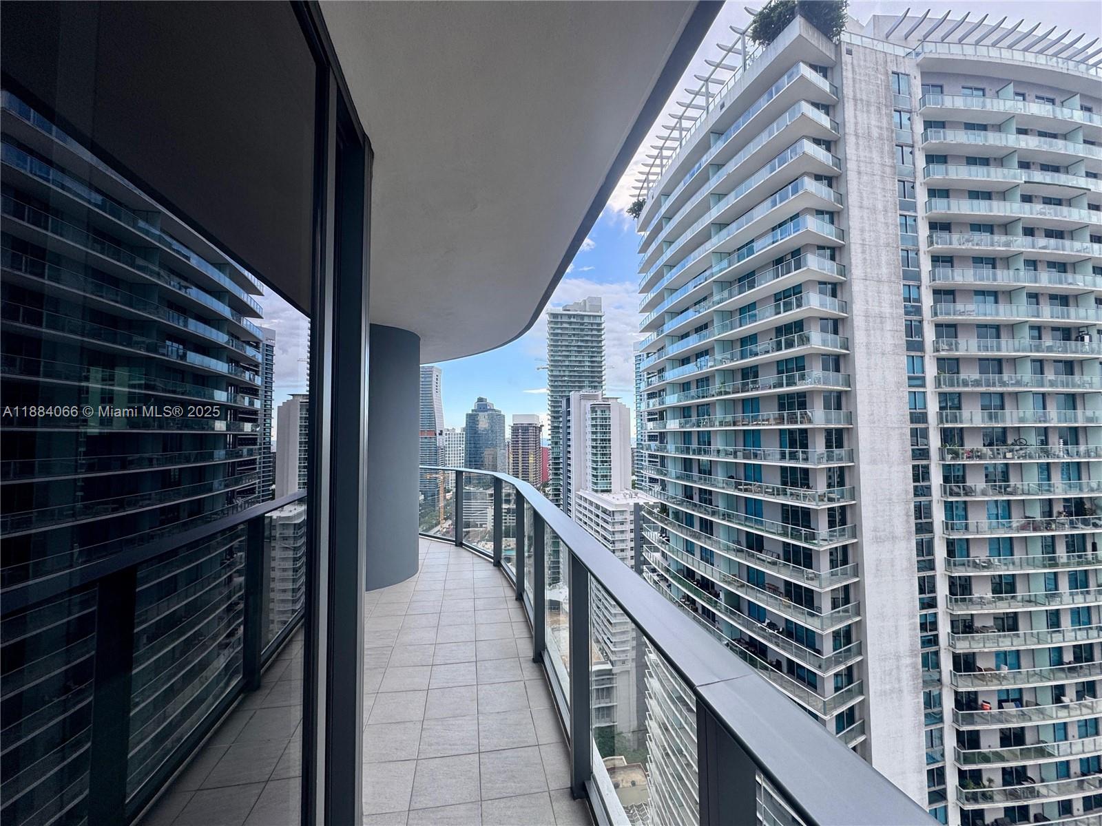 A curved balcony with tile flooring overlooks a dense urban skyline of high-rise buildings — 1000 Brickell Plz # 3302, Miami FL 33131, MIAMI, FL
