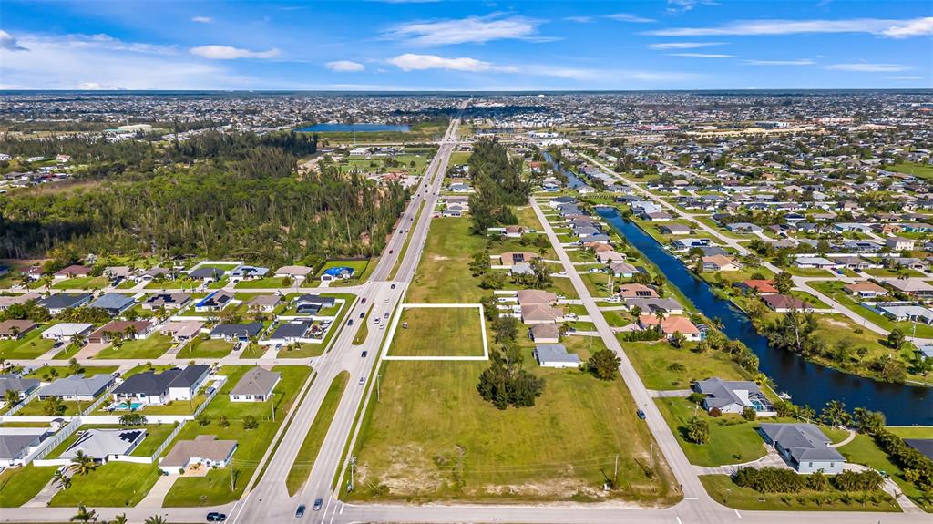An aerial view shows a vacant rectangular lot outlined in white next to a road — 1213 CHIQUITA BOULEVARD S, CAPE CORAL, FL