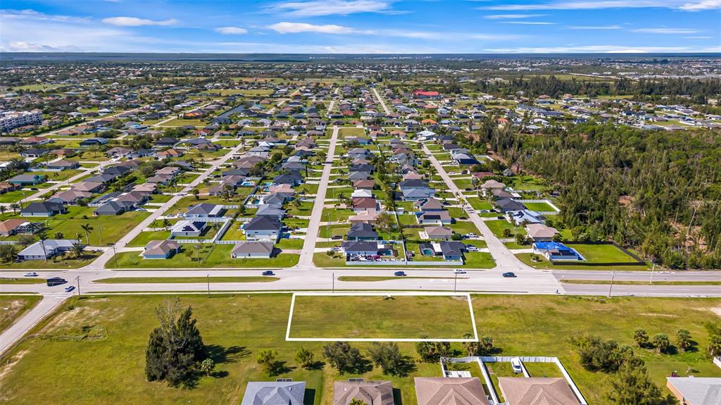 An aerial view shows a rectangular vacant lot outlined in white along a paved road — 1213 CHIQUITA BOULEVARD S, CAPE CORAL, FL