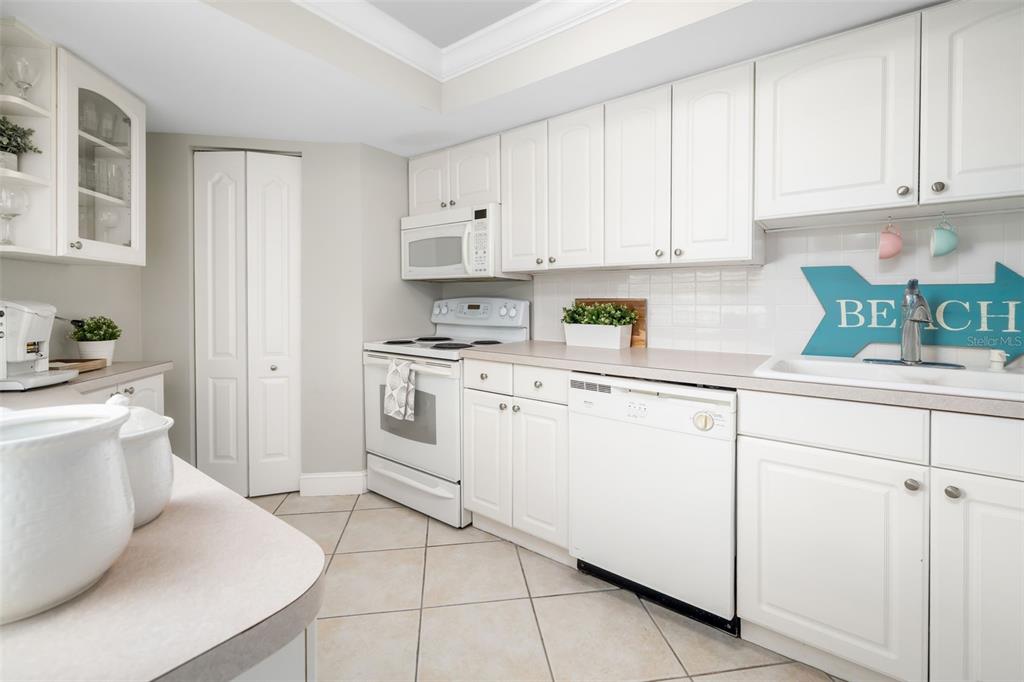 A white kitchen features tile flooring, white cabinetry, and a "BEACH" sign on the wall — 1770 BENJAMIN FRANKLIN DRIVE UNIT 203, SARASOTA, FL