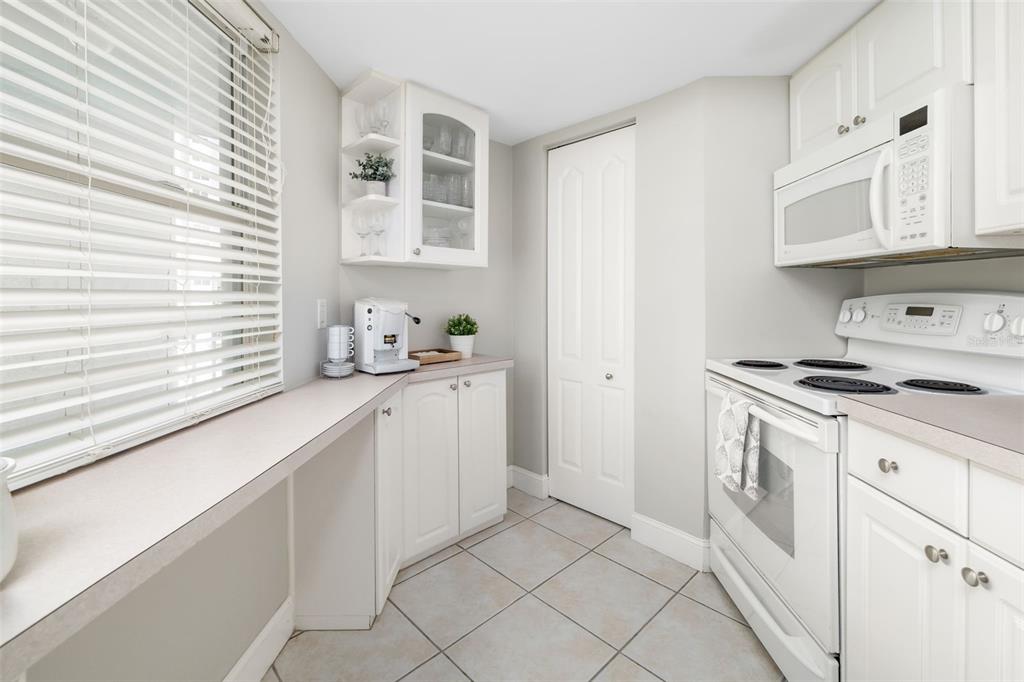 A kitchen features white cabinets, a white stove, a microwave, and a window with blinds — 1770 BENJAMIN FRANKLIN DRIVE UNIT 203, SARASOTA, FL