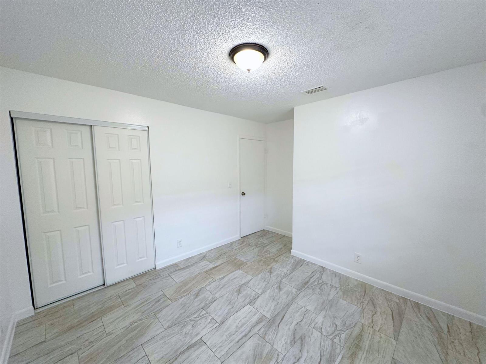 A bedroom with white walls, a sliding closet, a single door, and light-colored tile flooring — 329 Melody Lane, Lantana FL 33462, LANTANA, FL